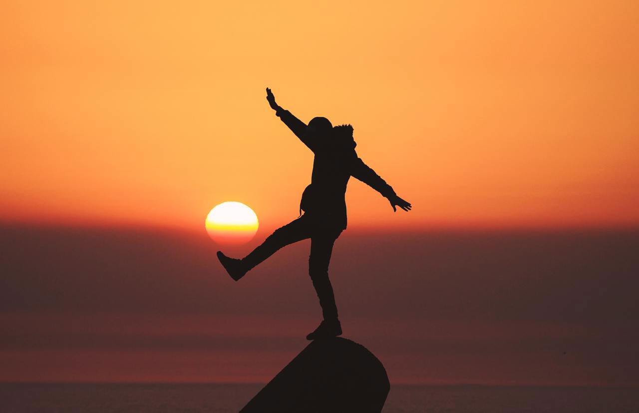 Person som balanserar på framfor ein solnedgang