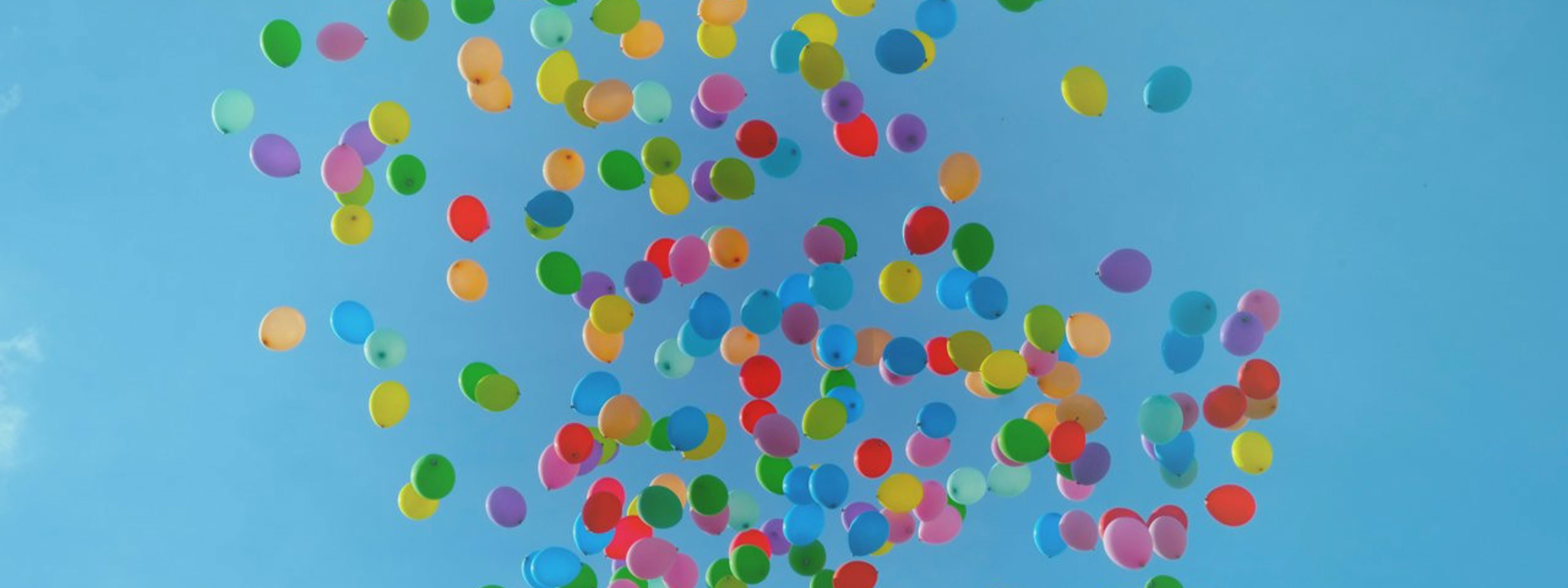 Hundrevis av fargerike ballonger som flyr mot ein blå knall himmel.